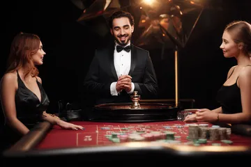 A professional dealer in a tuxedo greeting players at the roulette table, symbolizing the authentic live casino feel at GOOD112.