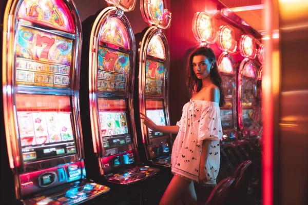 A stylish woman beside vibrant slot machines displaying glowing sevens, showcasing the variety of top slots at GOOD112.